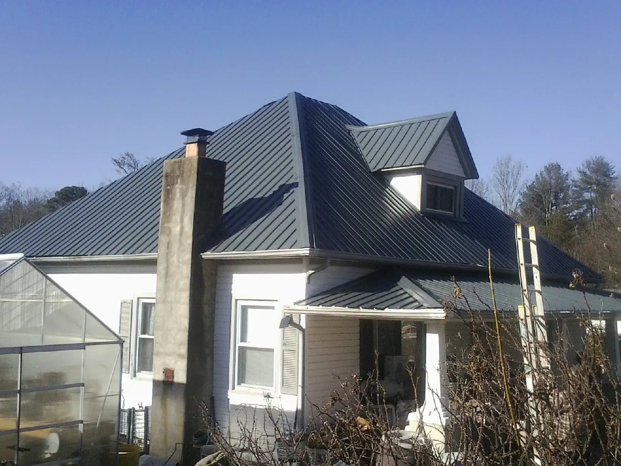 Dark blue standing seam metal roof on a white farmhouse with dormer — Slate & Tile Roof Repair by Roofing Brothers in Hartly