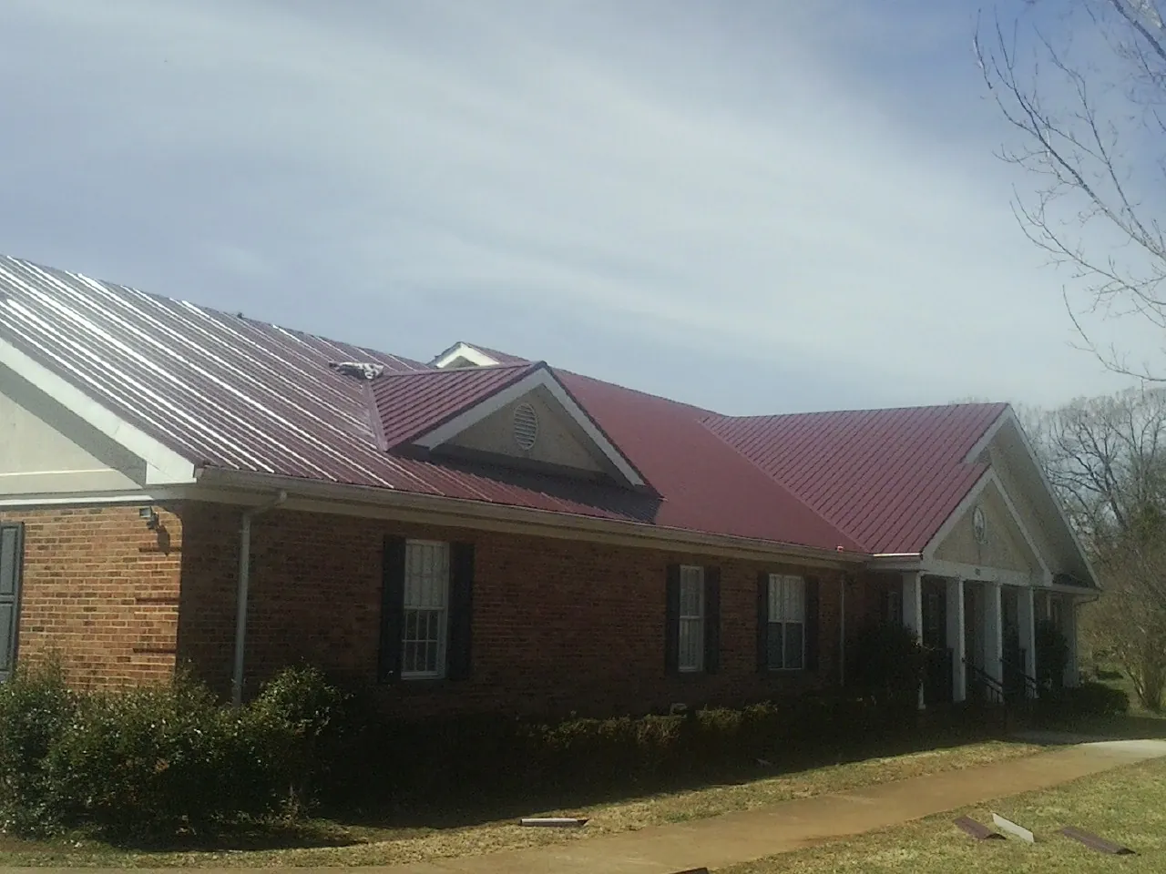 Red metal roof with gabled entries on a long brick building, from a Hail Damage Roof Repair job in Hartly