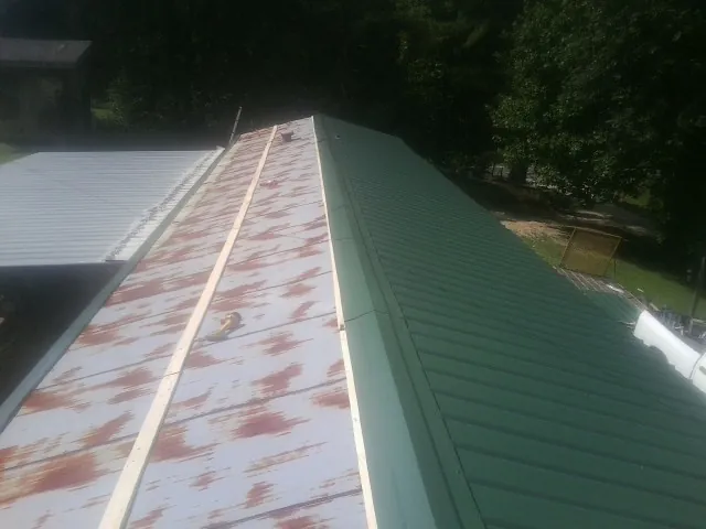 Old rusted panels beside newly installed green metal roofing — Wind Damage Roof Repair by Roofing Brothers in Hartly