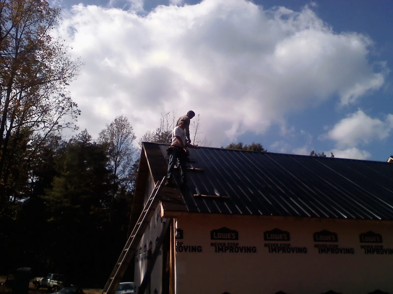 Roofer fastening dark metal panels high against a cloudy sky, from a Roof Inspection job in Hartly