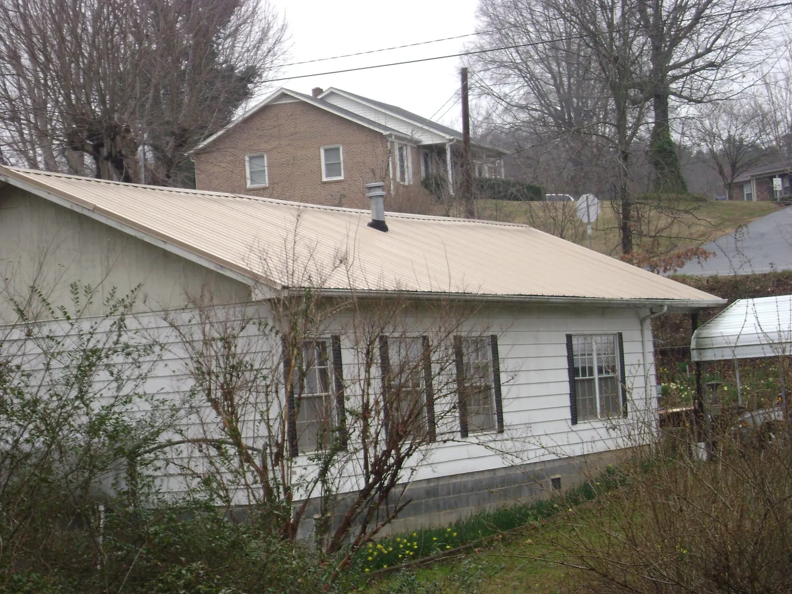 Tan metal roof on a white sided house set into a hillside — Commercial Roofing by Roofing Brothers in Hartly